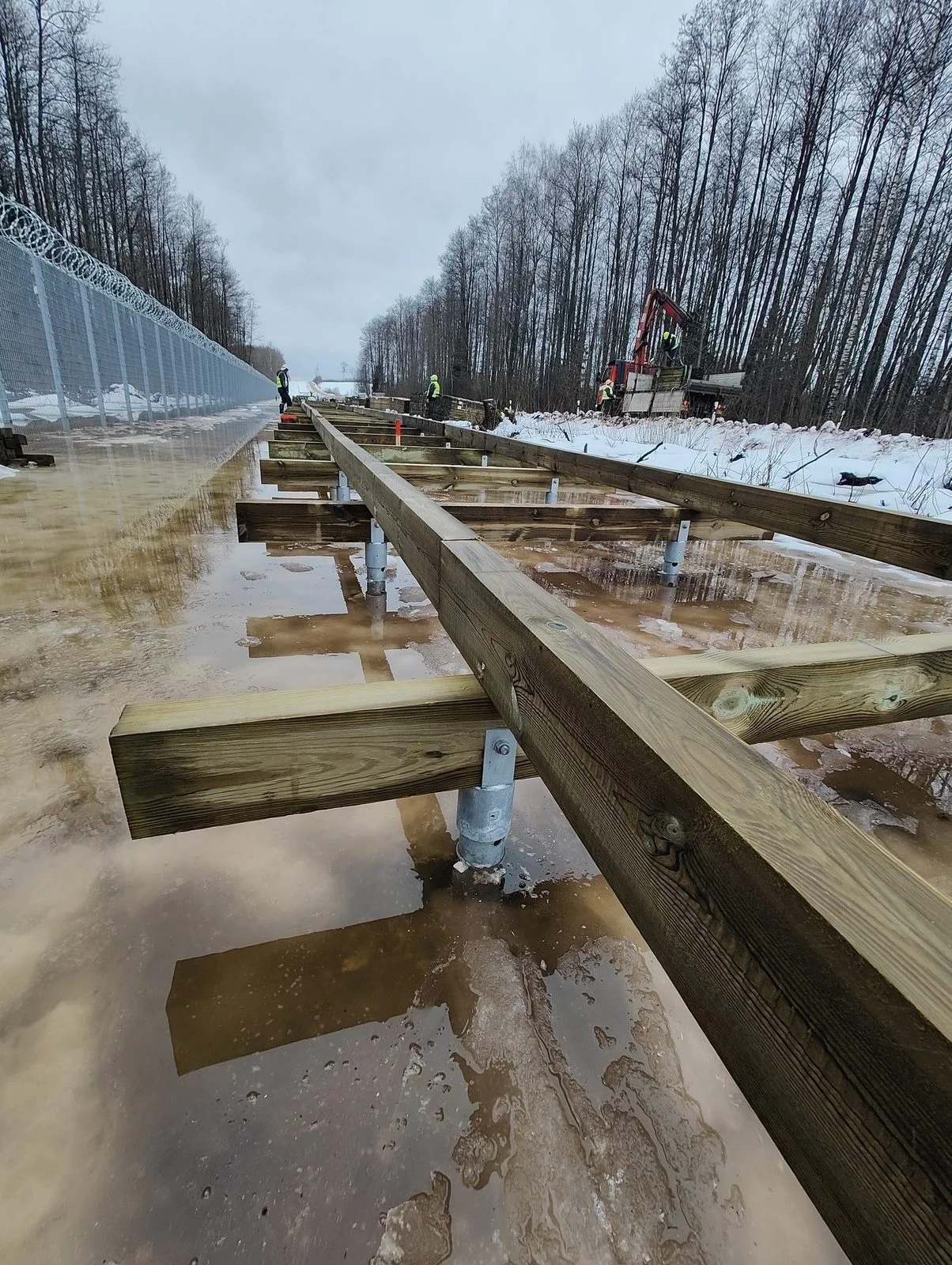 Estructura de pasarela de madera montada sobre soportes U de pilotes helicoidales durante la construcción de la pasarela fronteriza en Letonia