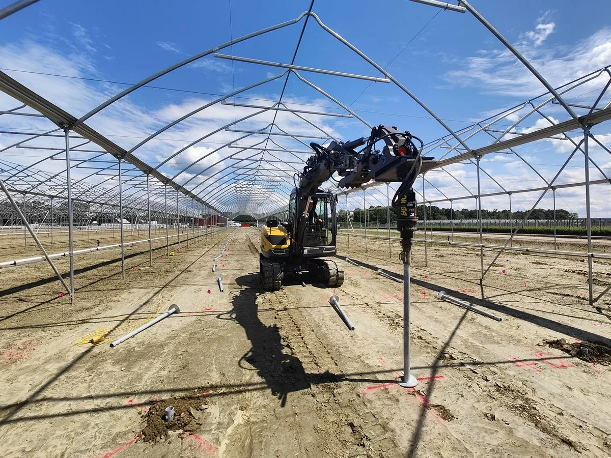 Excavadora instalando pilotes helicoidales bajo un invernadero tipo túnel